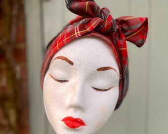May include: Red and black plaid headband with a bow tied on top. The headband is on a white mannequin head.