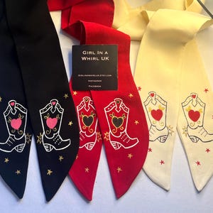 Peut inclure: Écharpes décoratives noires, rouges et crème. Chaque écharpe présente un motif de botte de cowboy avec un cœur et des étoiles. Les écharpes ont une extrémité pointue et conviennent à différents styles.