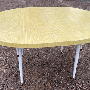 May include: A yellow oval-shaped table with white legs and gold accents. The table top has a wood grain pattern.
