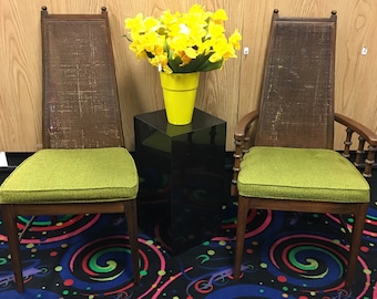 May include: Two wooden chairs with green upholstery and woven cane backs. The chairs are on a black and white patterned rug. A yellow vase with yellow flowers sits on a black pedestal in the center.