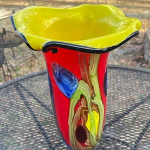 Könnte beinhalten: Eine farbenfrohe Glasvase mit gelber Oberseite und rotem, blauem, grünem und braunem Korpus. Die Vase hat einen gewellten Rand und ein einzigartiges, abstraktes Design.