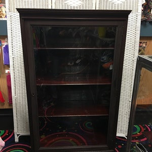 May include: A dark brown wooden display cabinet with glass doors and shelves. The cabinet has a traditional design with ornate details and sits on a colorful patterned floor.