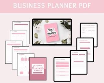 May include: A pink and white business planner with the text "Progress, not Perfection" and "Business Planner". The planner is surrounded by white cotton balls and green leaves. The planner is on a laptop screen.