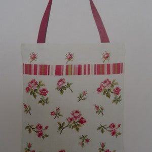 Könnte beinhalten: Eine weiße Einkaufstasche mit einem rosa-grünen Streifenband und einem Blumenmuster aus rosa Rosen. Die Tasche hat rote Henkel. Der Text "Sac Semis de Roses" befindet sich oben im Bild. Der Text "KIT CONTAINS / CE KIT CONTIENT:" befindet sich unten im Bild.