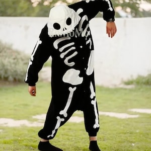 May include: A black skeleton onesie with white bone details. The onesie has a hood with a skull face.