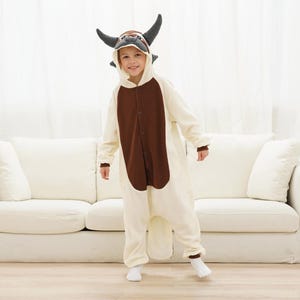 May include: A child wearing a white and brown animal onesie with a gray head and horns. The onesie has a button closure down the front.
