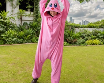 May include: A pink, hooded onesie with a cartoon character face on the hood. The onesie has a zipper down the front and red accents on the sleeves. The person is standing on green grass.