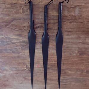 May include: Three identical black, pointed, spear-like tools with long, slender blades and cylindrical handles. Each handle features a textured grip and a small black loop at the top for hanging. The objects are arranged vertically in a parallel row.