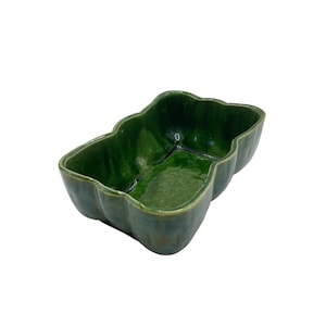 May include: A green ceramic planter with a wavy, organic shape. The planter is glazed and has a glossy finish.