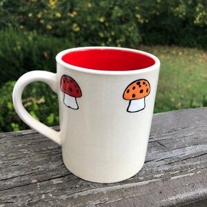 May include: White ceramic mug with a red interior and two black and orange mushroom illustrations.