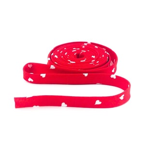 May include: A roll of red fabric trim with white heart print. The trim is rolled up and the end is laying flat.