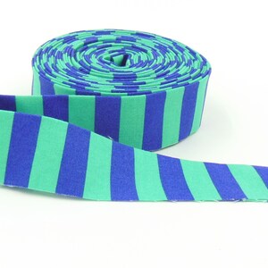 May include: A roll of fabric ribbon featuring a repeating pattern of vertical stripes in alternating shades of bright blue and mint green. The ribbon is coiled into a circular shape with one end extending outward, displaying the consistent striped design.