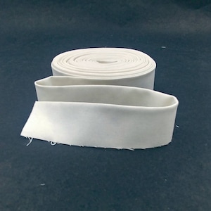 May include: A roll of white fabric trim, folded in half, with the edges of the fabric slightly frayed.