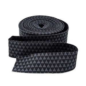 May include: A rolled-up length of fabric with a repeating triangle pattern in shades of gray and black. The fabric is folded over, creating a band. The pattern is visible on both the rolled portion and the unfolded section.