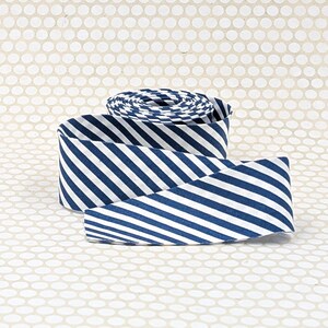 May include: A roll of fabric ribbon featuring a repeating pattern of diagonal navy blue and white stripes. The ribbon is coiled into a circular shape with a loose end extending forward, showcasing the consistent striped design throughout the material.