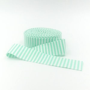 May include: A roll of fabric ribbon featuring a repeating pattern of vertical mint green and white stripes. The ribbon is coiled into a circular shape with one end extending outward, displaying the consistent striped design across the entire surface.