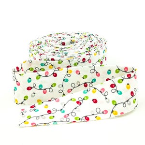 May include: A roll of white fabric with a repeating pattern of colorful Christmas lights. The lights are red, green, yellow, and pink, connected by a black wire. The fabric is unrolled in a section, showing the pattern.