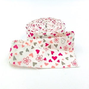 May include: A roll of white fabric with a pink and gray heart and flower pattern.