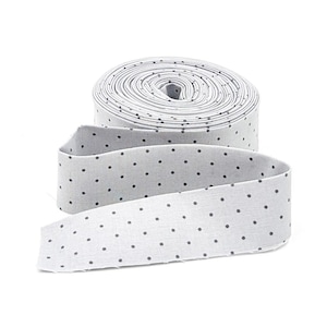 May include: A roll of light gray fabric ribbon featuring a repeating pattern of small, dark gray polka dots. The ribbon is wound into a tight circular coil with one end extending outward, displaying the consistent dotted design across the surface.