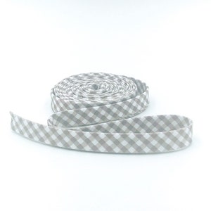 May include: A roll of beige and white gingham ribbon. The ribbon is folded and rolled into a coil.
