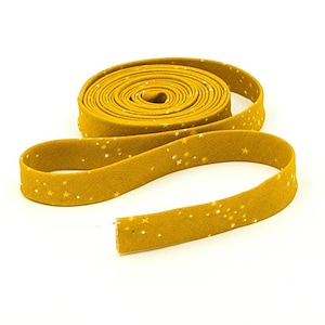 May include: Mustard yellow bias tape, rolled and unrolled, with a repeating pattern of small white stars. The fabric is a solid color with a subtle texture. The tape is used for sewing and crafting projects.