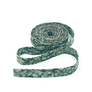 May include: A roll of green and black patterned fabric ribbon. The ribbon has a speckled pattern.