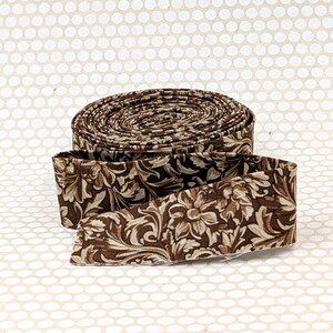 May include: A roll of brown fabric with a floral pattern in shades of brown and cream. The fabric is unrolled at the bottom, revealing the pattern. The fabric is likely used for sewing or crafting projects.