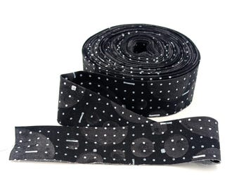 May include: A roll of black and white patterned fabric ribbon with white polka dots and geometric shapes. The ribbon is rolled up and ready to be used for crafting or sewing projects.