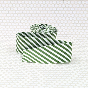 May include: A roll of fabric ribbon featuring a repeating diagonal stripe pattern in forest green and white. The ribbon is coiled at the top with a length extending forward, showcasing the consistent angled lines across the woven textile surface.