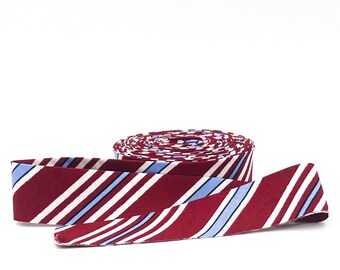 May include: A roll of red and white striped fabric with blue stripes. The fabric is rolled up and the end of the roll is unfurled.