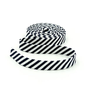 May include: A roll of navy blue and white striped bias tape. The tape is coiled in a spiral, with a portion unraveled and extending outward. The stripes are evenly spaced and angled across the tape.