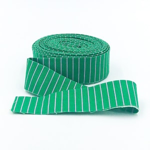 May include: A roll of green and white striped fabric ribbon. The ribbon is rolled up and a section is unrolled to show the pattern.