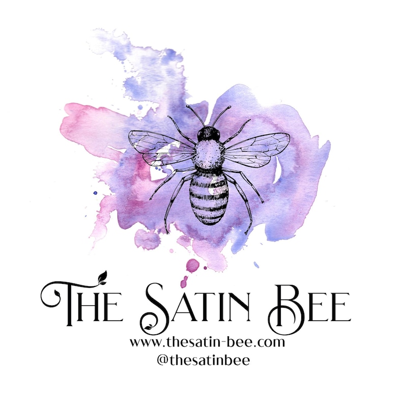 May include: A black ink illustration of a bee centered over a purple and pink watercolor splash. Below the bee, the text reads THE SATIN BEE in a decorative font, followed by the website www.thesatin-bee.com and the handle @thesatinbee.