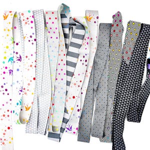 May include: A collection of fabric strips in various patterns and colors. Designs include geometric shapes, polka dots, stripes, and stars. Colors include white, gray, black, and a variety of bright colors. The strips are likely for crafting or sewing projects.