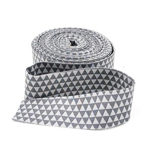 May include: A roll of gray and white patterned fabric with a repeating triangle design. The fabric is unrolled in the foreground, revealing the pattern. The fabric is likely used for sewing or crafting projects.
