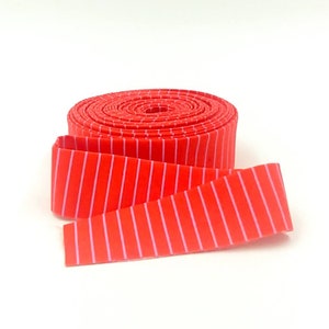 May include: A roll of red and pink striped fabric ribbon. The ribbon is rolled up and the end is unfurled, showing the striped pattern.
