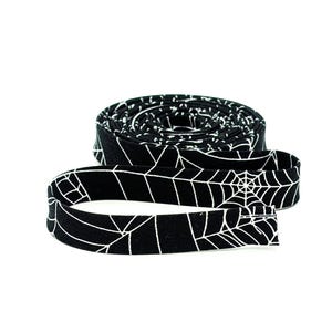 May include: A black fabric strip with a white spiderweb design, rolled up and partially unrolled. The fabric is likely cotton or a similar material, suitable for crafting or decorative purposes. The spiderweb pattern is a Halloween or gothic theme.