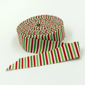 May include: A roll of fabric ribbon featuring a repeating vertical stripe pattern in alternating colors of bright red, grass green, and crisp white. The ribbon is wound into a tight circular coil with one end extending outward to show the pattern.