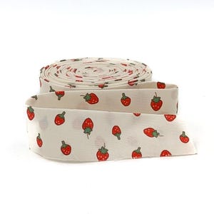 May include: A roll of white fabric with a repeating pattern of red strawberries with green stems. The fabric is unrolled, revealing the strawberry design. The fabric is likely used for sewing, crafting, or other DIY projects.