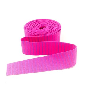 May include: A roll of pink and purple striped elastic trim. The trim is rolled up and the end is unfurled.