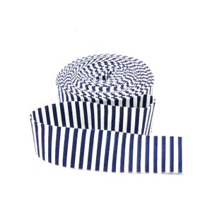 May include: A roll of fabric ribbon featuring a repeating pattern of vertical navy blue and white stripes. The ribbon is coiled into a circular shape with one end extending outward, displaying the consistent striped design across the entire length.