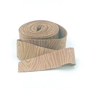 May include: A roll of brown fabric ribbon with a woodgrain pattern. The ribbon is rolled up and has a loose end.