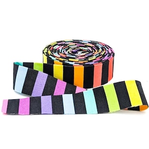May include: A roll of fabric tape featuring a repeating pattern of vertical stripes in alternating black and vibrant colors including neon yellow, orange, pink, purple, and light blue. The tape is coiled into a flat cylinder with one end extended.