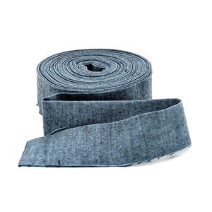 May include: A roll of blue denim fabric with a lighter blue edge. The fabric is rolled up in a spiral, with a length of the fabric unrolled and lying flat. The fabric has a textured appearance.