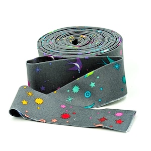 May include: A roll of gray fabric with a colorful celestial pattern. The fabric features stars, circles, and a purple bird design. The fabric is unrolled, showing the pattern in detail.