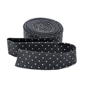 May include: A roll of black fabric with a white polka dot pattern. The fabric is unrolled in a length, showing the pattern clearly. The fabric is likely used for sewing or crafting projects.