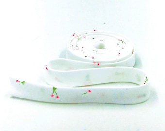 May include: White elastic trim with a small cherry print. The trim is rolled up and ready to be used for sewing projects.