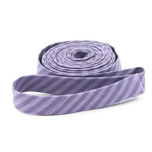 May include: A roll of lavender and light purple bias tape featuring a diagonal striped pattern. The fabric trim is coiled into a circular shape with one end extending outward, showcasing the woven texture and consistent striped design throughout.