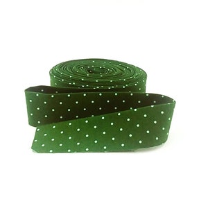 May include: A roll of dark green ribbon with a repeating pattern of small white polka dots. The ribbon is unrolled in the foreground, revealing the pattern and texture. The background is plain white.