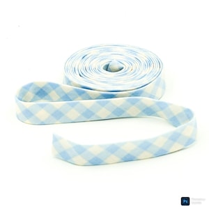 May include: A roll of light blue and white gingham fabric ribbon. The ribbon is unrolled in a curved line in the foreground, with the rolled portion in the background. The fabric has a soft, textured appearance.